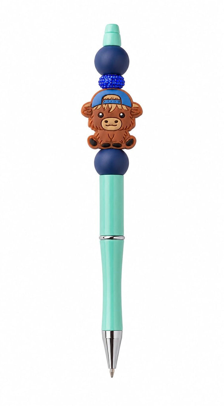 A teal custom ballpoint pen topped with a backward baseball cap Highland cow silicone charm, a glittering royal blue rhinestone spacer, and navy beads.