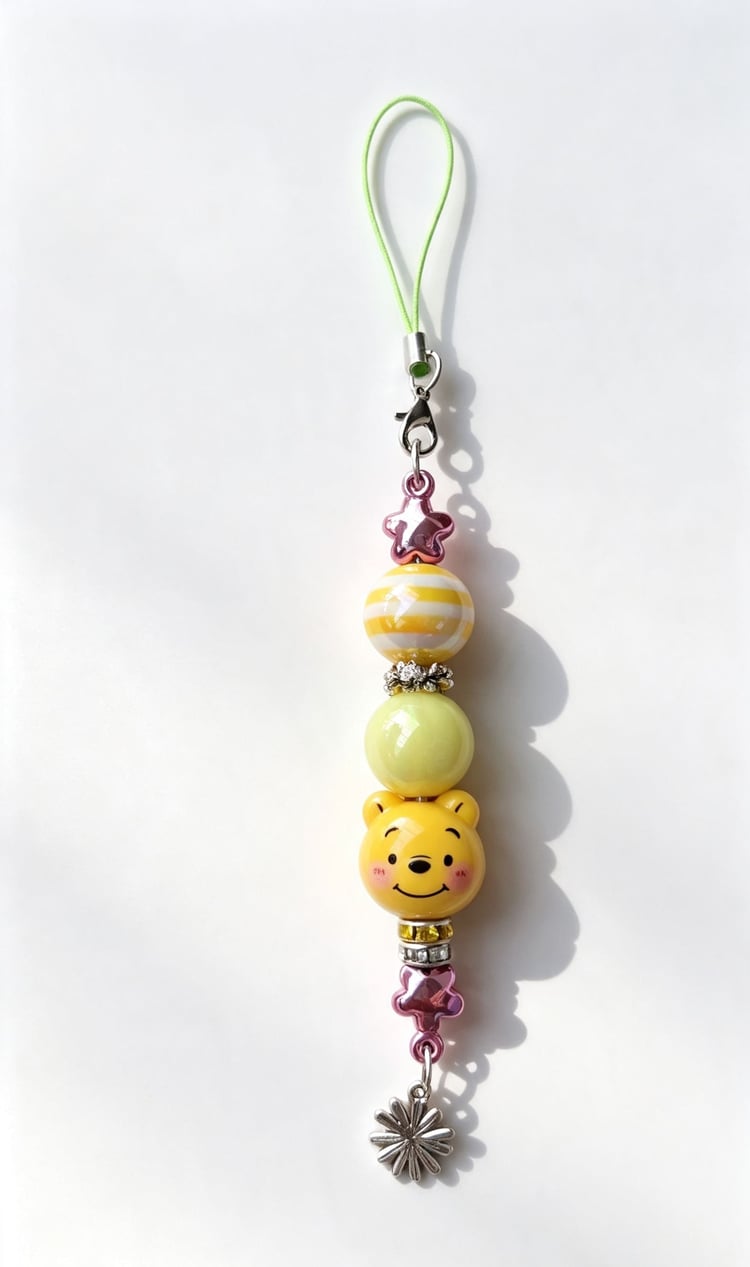 Close-up layout of a custom yellow bear phone charm by Sparkling Resin Delights, featuring a smiling cartoon bear silicone focal bead, pastel yellow and striped accent beads, crystal rhinestone spacers, metallic pink star beads, and a silver flower charm