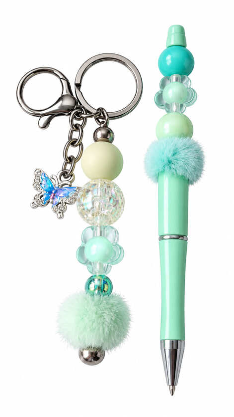 A luxury mint green stationery set showing a matching keychain and ballpoint pen, featuring a crystal-accented blue and purple butterfly charm, a clear crackle bead, flower-shaped beads, and fuzzy mint pom-poms.