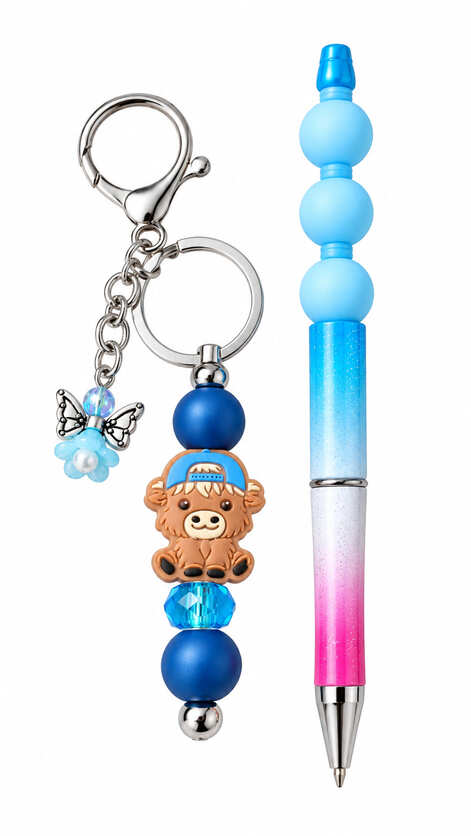 A cute blue and pink ombre stationery set showing a matching keychain and ballpoint pen, featuring a brown cartoon highland cow bead wearing a blue backwards cap, navy blue accents, and a dangling light blue flower butterfly charm.