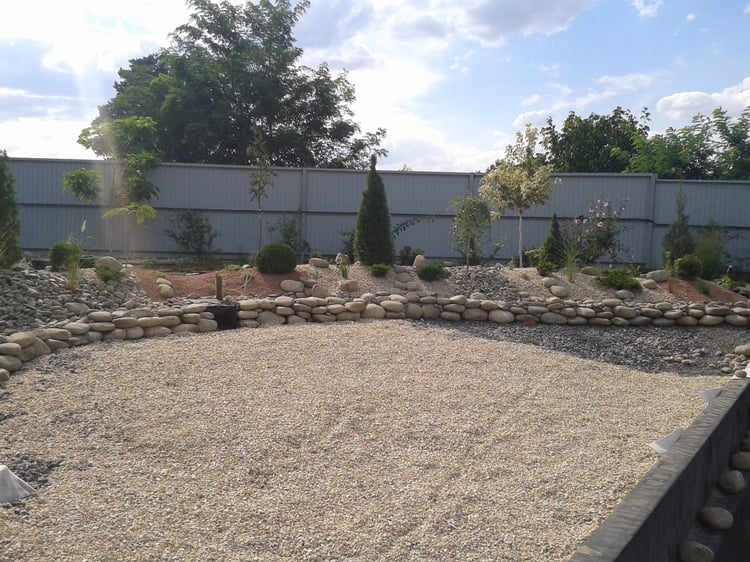 Natural swimming pond construction showing shoreline landform modelling, slope stabilisation, stone finishing and preparation of planted earth mounds in a large private garden.