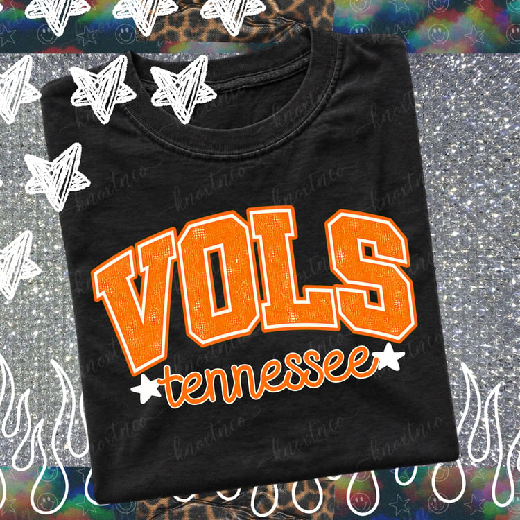 Folded black t-shirt featuring a distressed orange collegiate "VOLS" graphic with retro script "tennessee" and white star accents, displayed flat lay for Knoxville game day apparel.