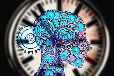 stock image of a human figure transposed over a watch face, with the figure being of a head made up of gears to represent the working of the mind and time