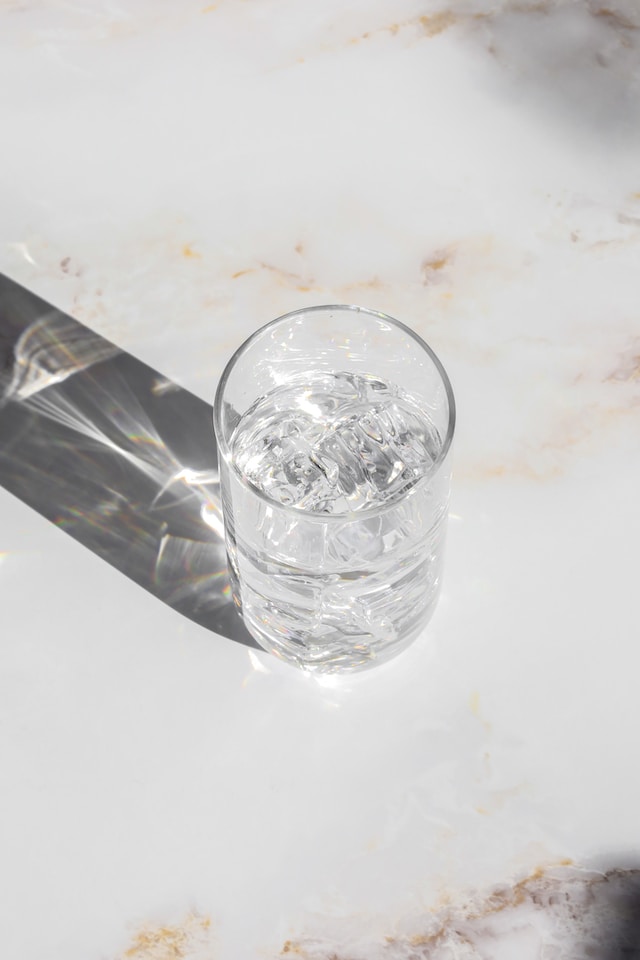 glass of ice water on a marble table sitting in the sun