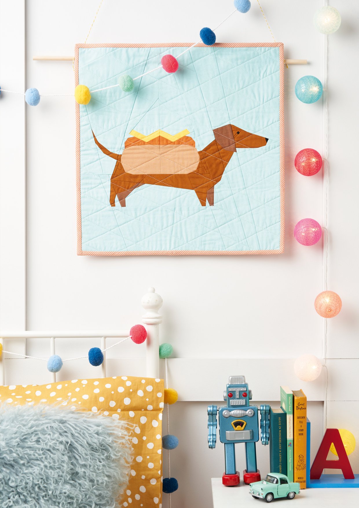 An image of my mini quilt in the shape of an adorable sausage dog, featured in Love, Patchwork & Quilting magazine, issue 126. The project measures 18" x 18" and is filled with vibrant colors and charming details.