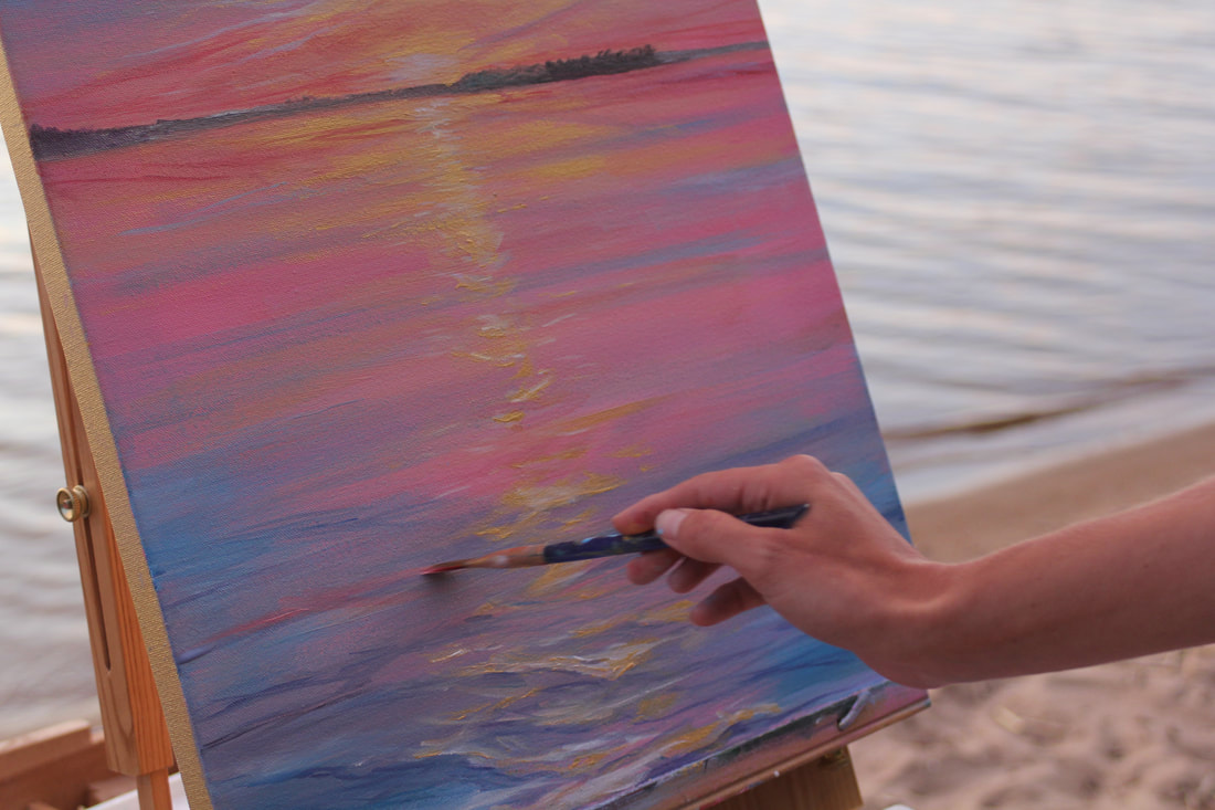 Artist painting a sunset painting while blending the colors of the water and sky.