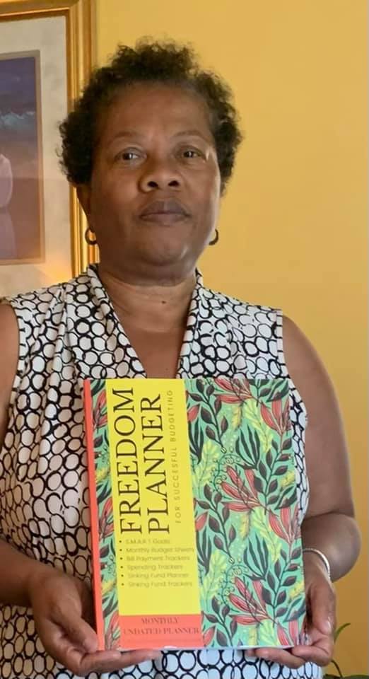Black woman with short hair holding up Freedom Planner with serious expression. Plan Your Freedom UGC image