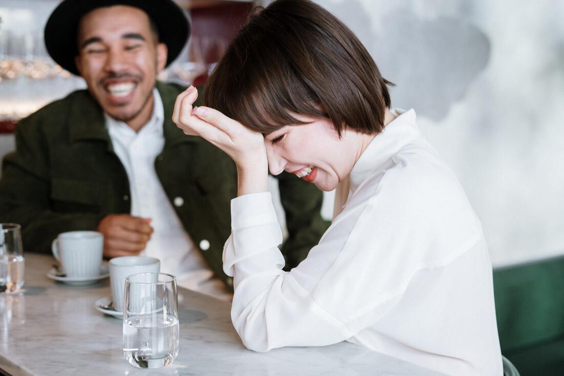 Man in a black hat laughing with woman in a white shirt