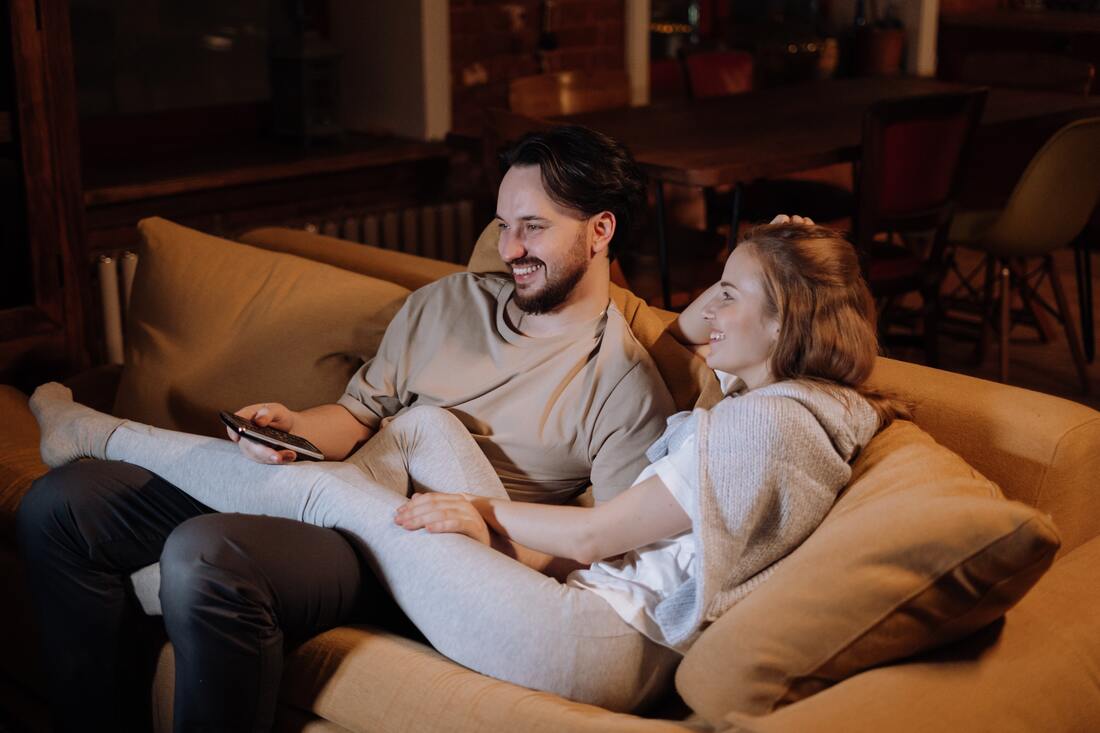 A couple sitting on a couch smiling watching television