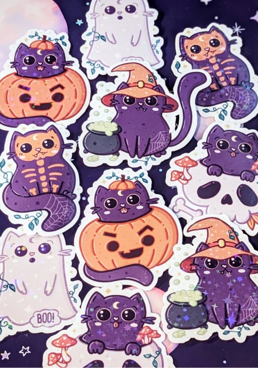 A sticker sheet with Halloween-themed illustrations. It includes purple cats dressed as skeletons and witches, a pumpkin with a cat's face, a ghost cat with the text "BOO!", and a cat with a cauldron. The design features cute, playful characters, with some stickers showcasing spooky elements like skulls, mushrooms, and webs, all in soft pastel colors with a whimsical, Halloween vibe.