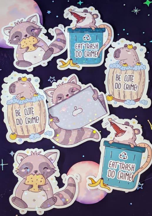 A sticker sheet with seven cute animal stickers. The stickers include a capybara in a barrel with bubbles, a raccoon holding a cookie, a raccoon hiding behind a laptop, and an opossum sitting in a trash can. Each sticker features the phrase "Be Cute Do Crime" or "Eat Trash Do Crime." The design uses soft pastel colors and playful illustrations.
