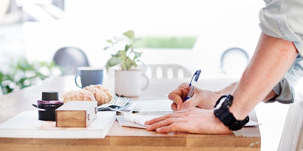 photo of standing person writing with pen at desk