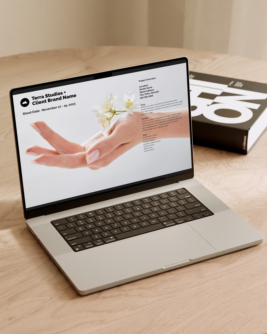 A laptop on a wooden table displays a presentation slide featuring an image of a hand delicately holding small flowers. A black and white box with numbers is in the background. The slide includes text, likely outlining project details.