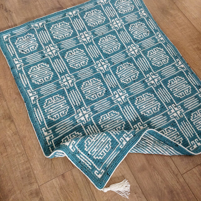 Crocheted blanket in cream and teal showing the Chinese Longevity symbol
