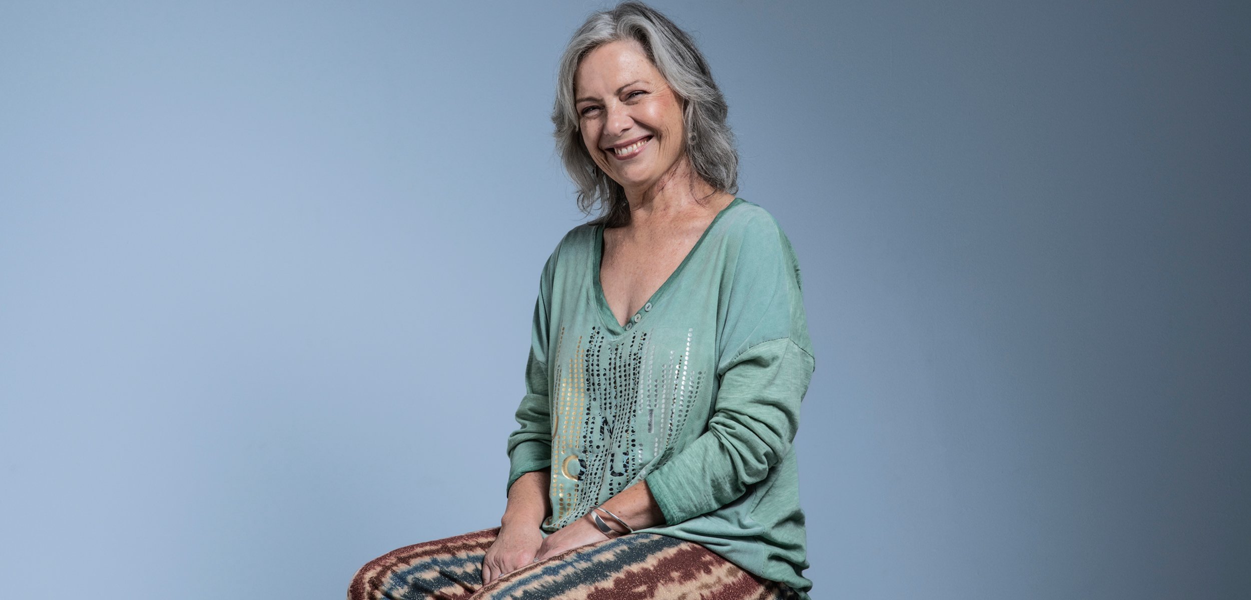 Female head and neck cancer survivor smiling and sitting on a stool