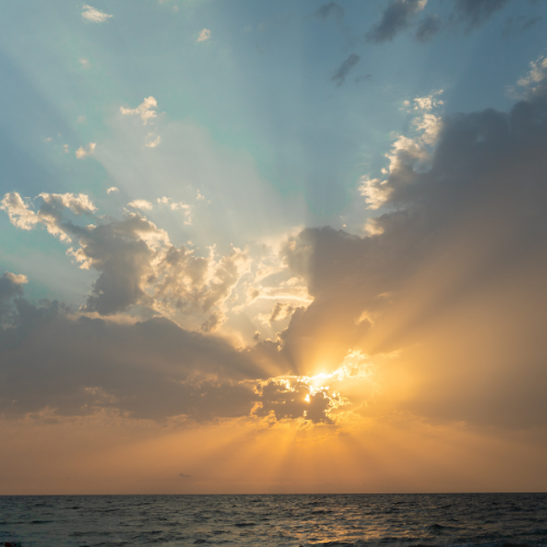 A breathtaking sunset over the ocean, with golden rays of sunlight piercing through scattered clouds.