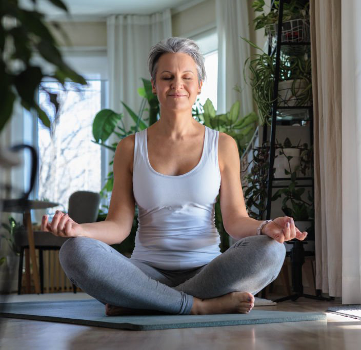 a woman sitting in meditation on her living room floor relaxed