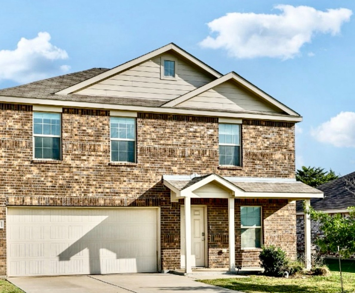 Two-story brick home with a double garage, covered entryway, and clean landscaping under a blue sky — perfect example of a well-maintained investment property.