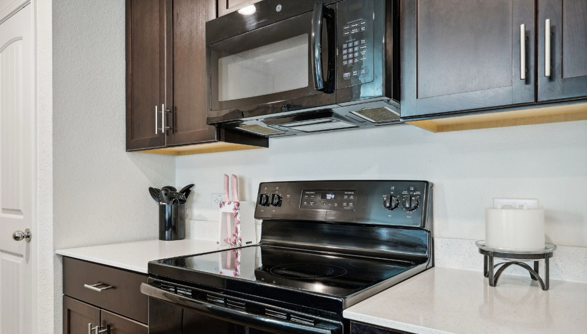 Close-up of a modern kitchen with dark wood cabinets, a black electric stove and microwave, and white quartz-style countertops — showcasing a clean, functional cooking space.