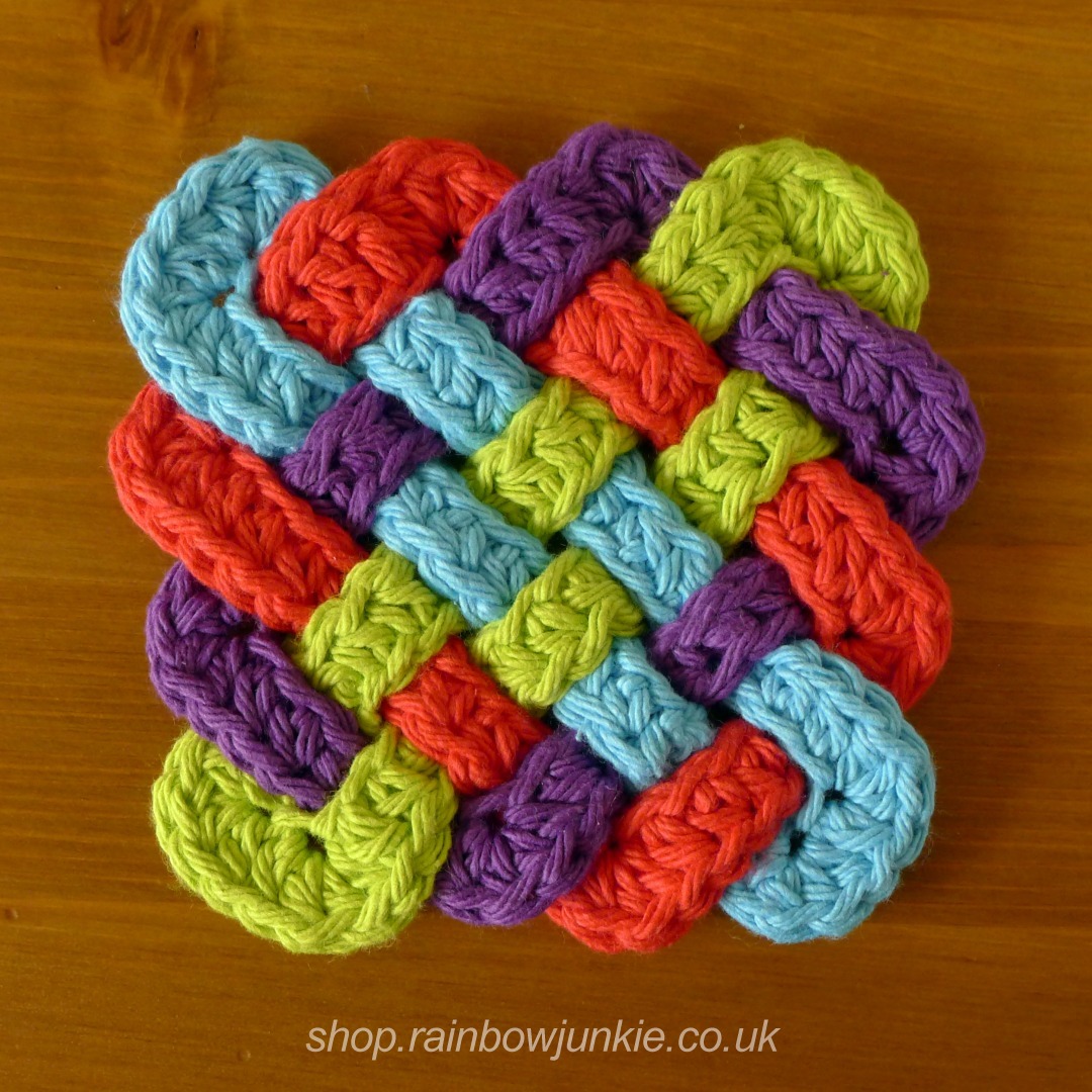 Four part Celtic plaitwork coaster made in worsted weight yarn in red, blue, green and purple.