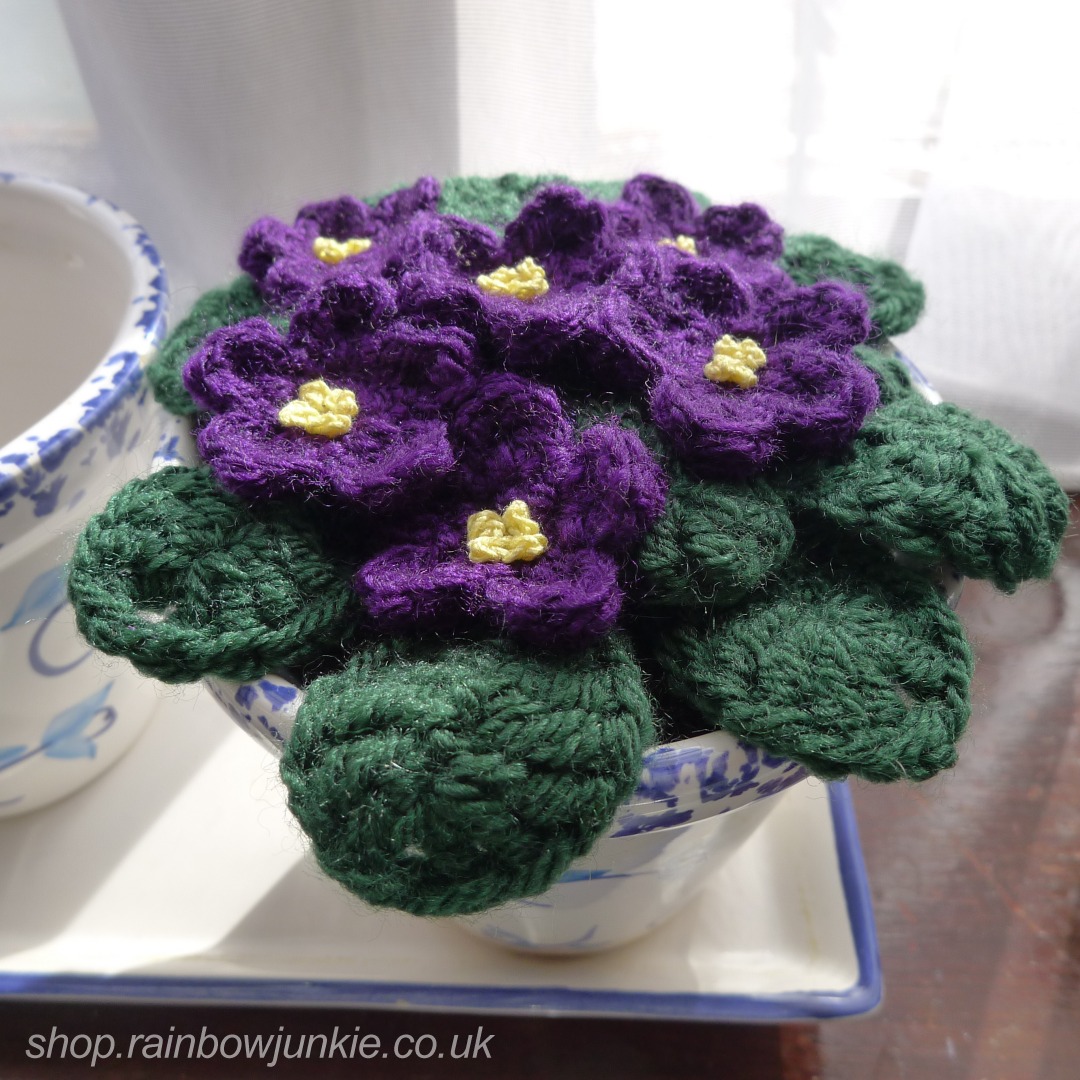 Dark purple crochet African violets on a window sill.