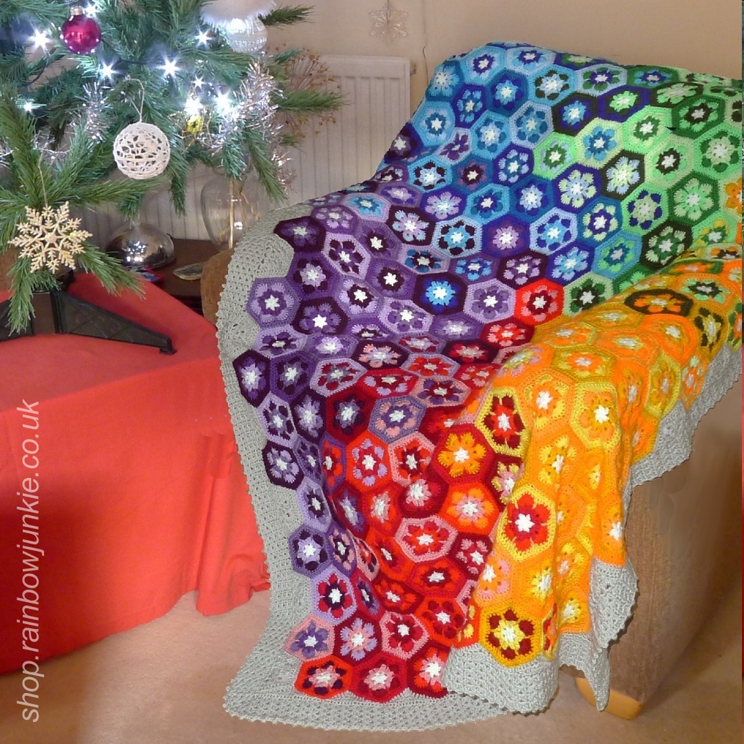 A blanket made of African flower hexagons in a swirl of rainbow colours with white snowflake centres.