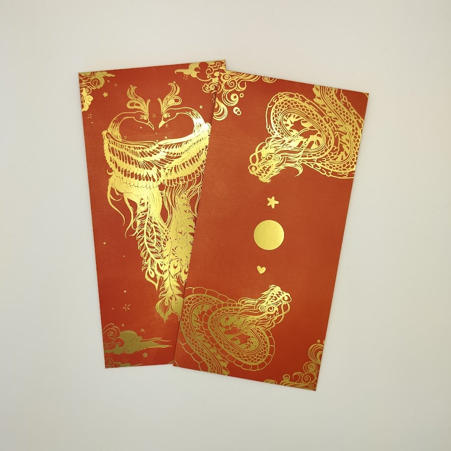 A hand holding two red hongbaos against a light background. The left hongbao has two dragons in gold foil, while the right has two phoenixes in gold foil. Both designs are ornate and detailed.