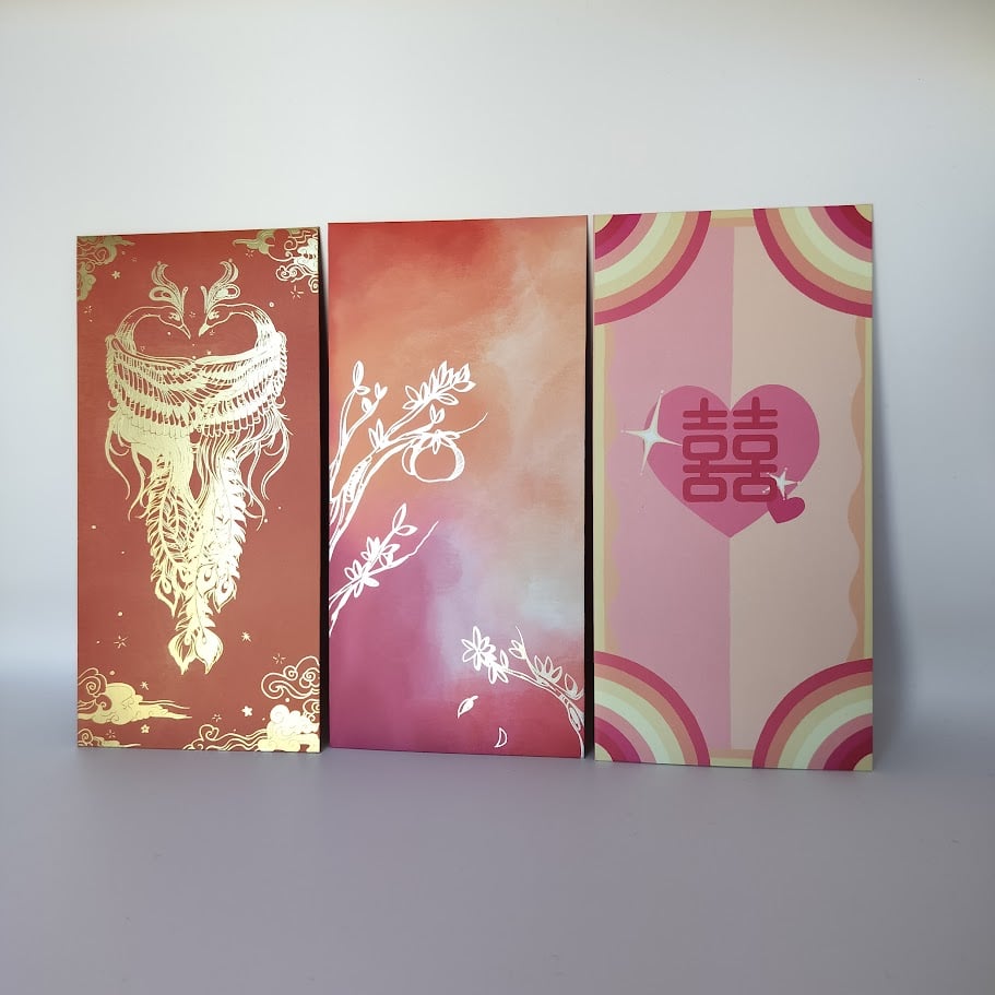 Three Chinese money envelopes (hongbao) in a row - a red envelope with gold phoenix design, an orange-to-purple gradient envelope with silver botanical foil, and a pink rainbow striped envelope with double happiness heart symbol.