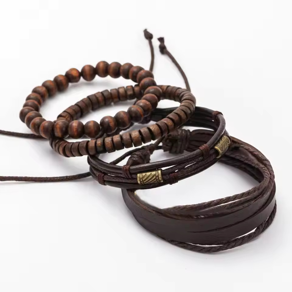 4-piece mens brown bracelet set, loosely arranged on a white background, featuring: two wooden bead bracelets (one with round beads, one with disc beads), one multi-strand dark brown leather cord bracelet with antique brass-tone metal tube accents, and o