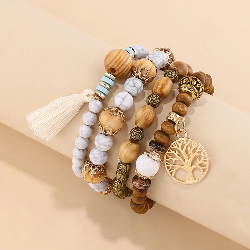 Stacked ladies multi-strand beaded bracelet set featuring a prominent gold-tone Tree of Life charm, a cream tassel, and a mix of natural brown wood beads, white howlite-style stone beads, turquoise accents, and antique gold-tone decorative metal beads. B