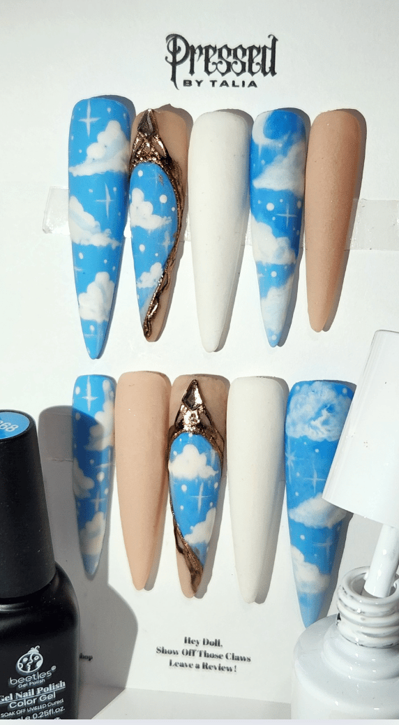 Extra extra long stiletto shaped handmade press-on nails with sky blue and cloud designs, customizable with white and nude acrylic nails, gold chrome baroque style accent press-on nails, displayed next to a bottle of white gel polish and baby blue gel pol