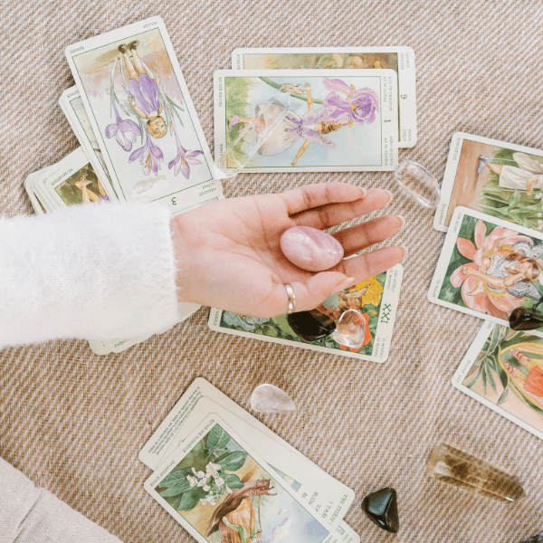 A hand holding rose quartz over a soft beige surface scattered with floral tarot cards and crystals, evoking gentle intuition and spiritual insight — image for Intuitive Tarot Readings page on iamisabelbar.com