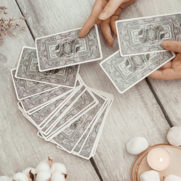 Hands shuffling a spread of tarot cards on a rustic wooden table with cotton and candles, illustrating intuitive tarot reading — on the Work With Me page of iamisabelbar.com