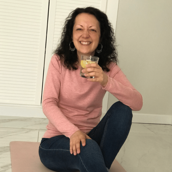 Isabel Bar smiling warmly and holding a glass of lemon water, sitting cross-legged — Contact page on iamisabelbar.com