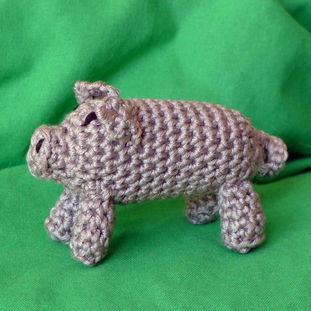 A side view of a grey crochet pig against a green background.