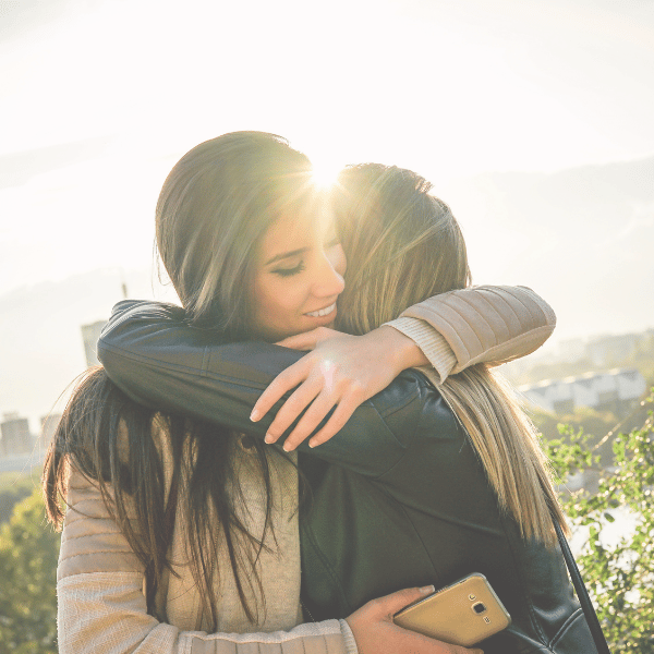 Two women embracing in warm sunlight outdoors, symbolizing connection and support — on the Work With Me page of iamisabelbar.com