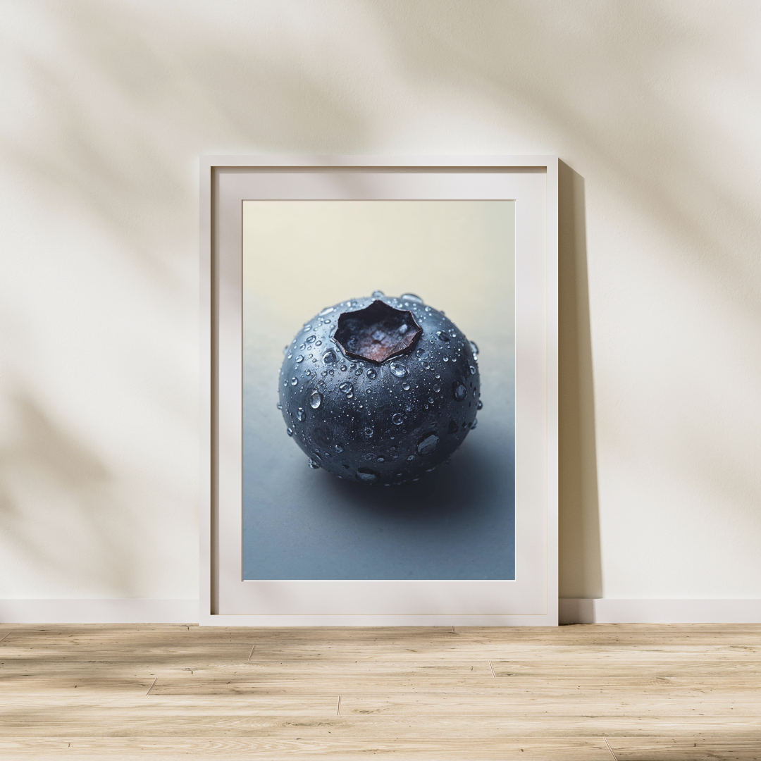 A close-up photograph of a single fresh blueberry covered in small water droplets. The berry has a smooth, dark blue surface with a matte sheen and a star-shaped calyx at the top. The soft lighting and neutral background highlight the texture and moisture