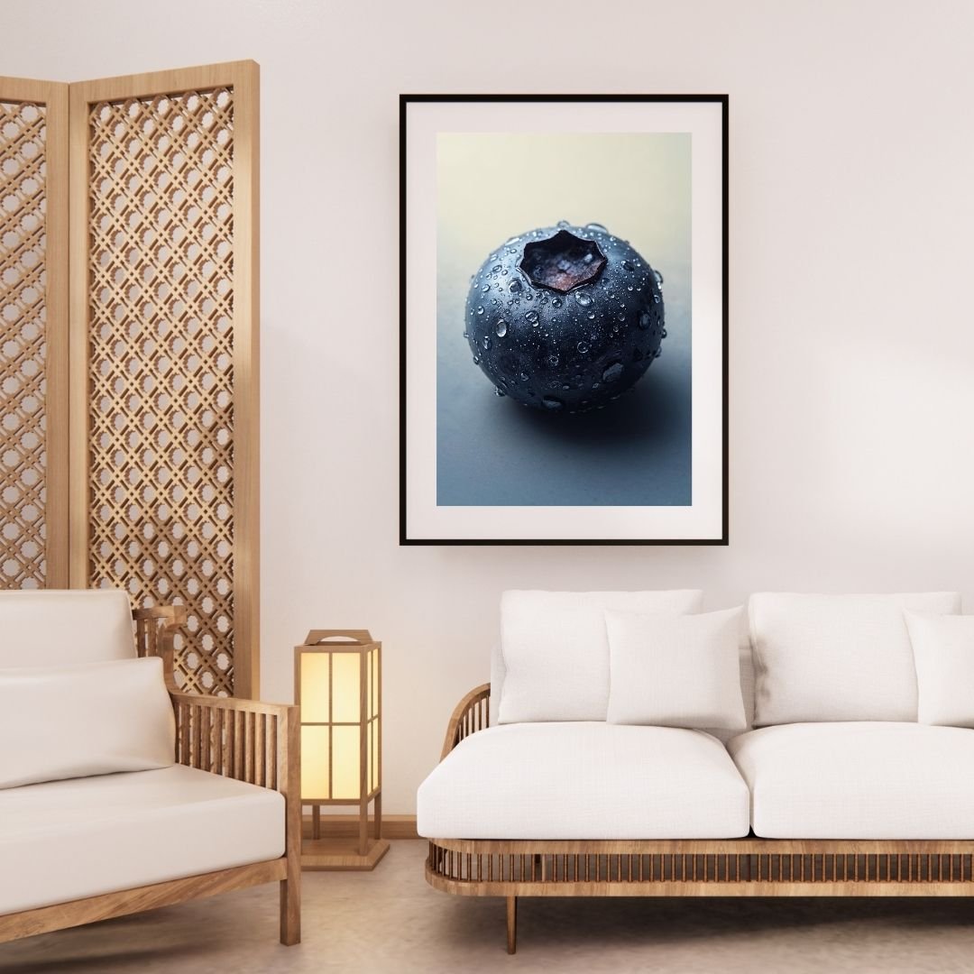A close-up photograph of a single fresh blueberry covered in small water droplets. The berry has a smooth, dark blue surface with a matte sheen and a star-shaped calyx at the top. The soft lighting and neutral background highlight the texture and moisture