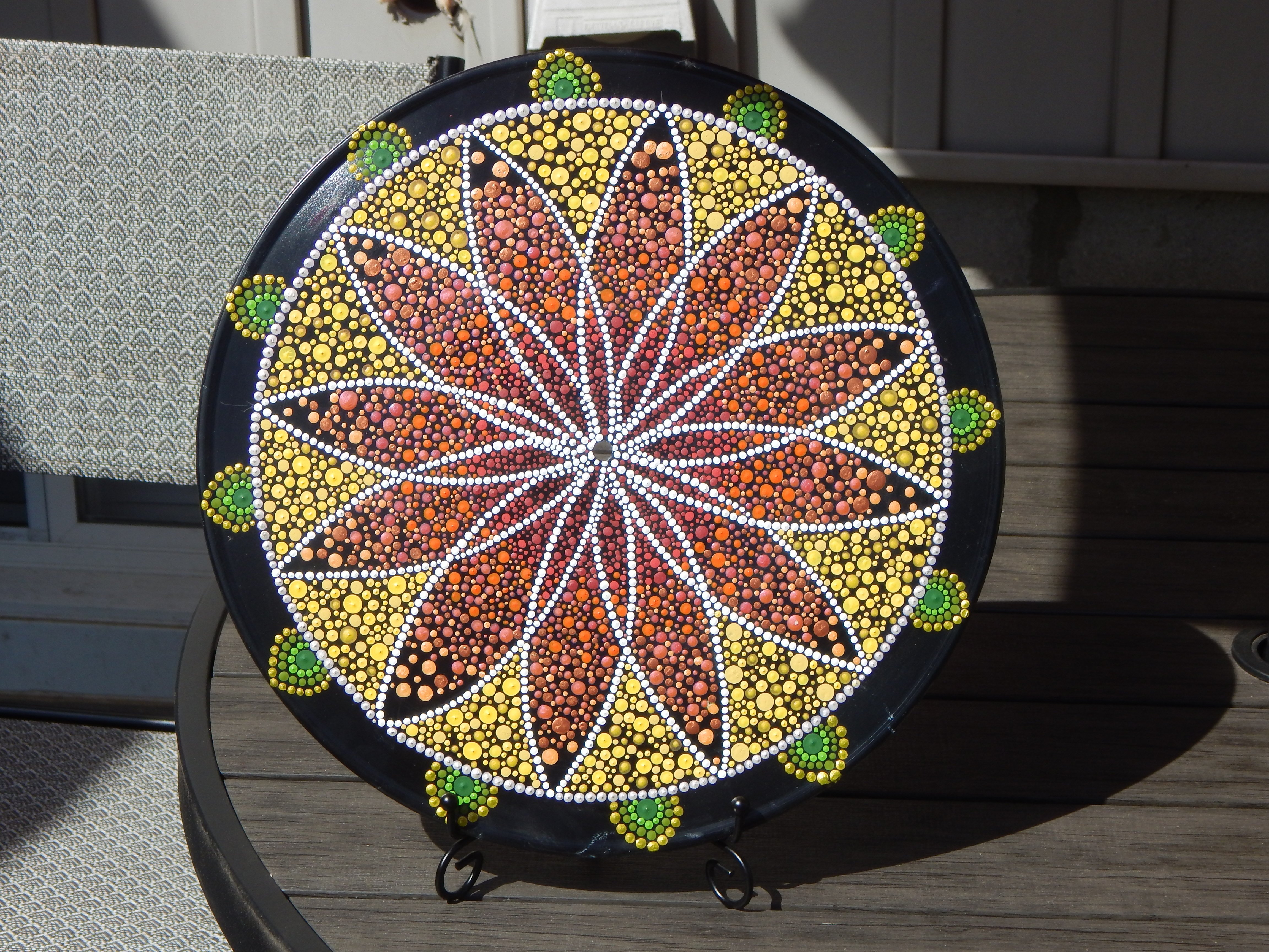 Hand-painted dot mandala on upcycled vinyl record featuring bold petal design in warm yellow, orange, and green tones. Vibrant boho wall art with retro flair, crafted using dot painting techniques.