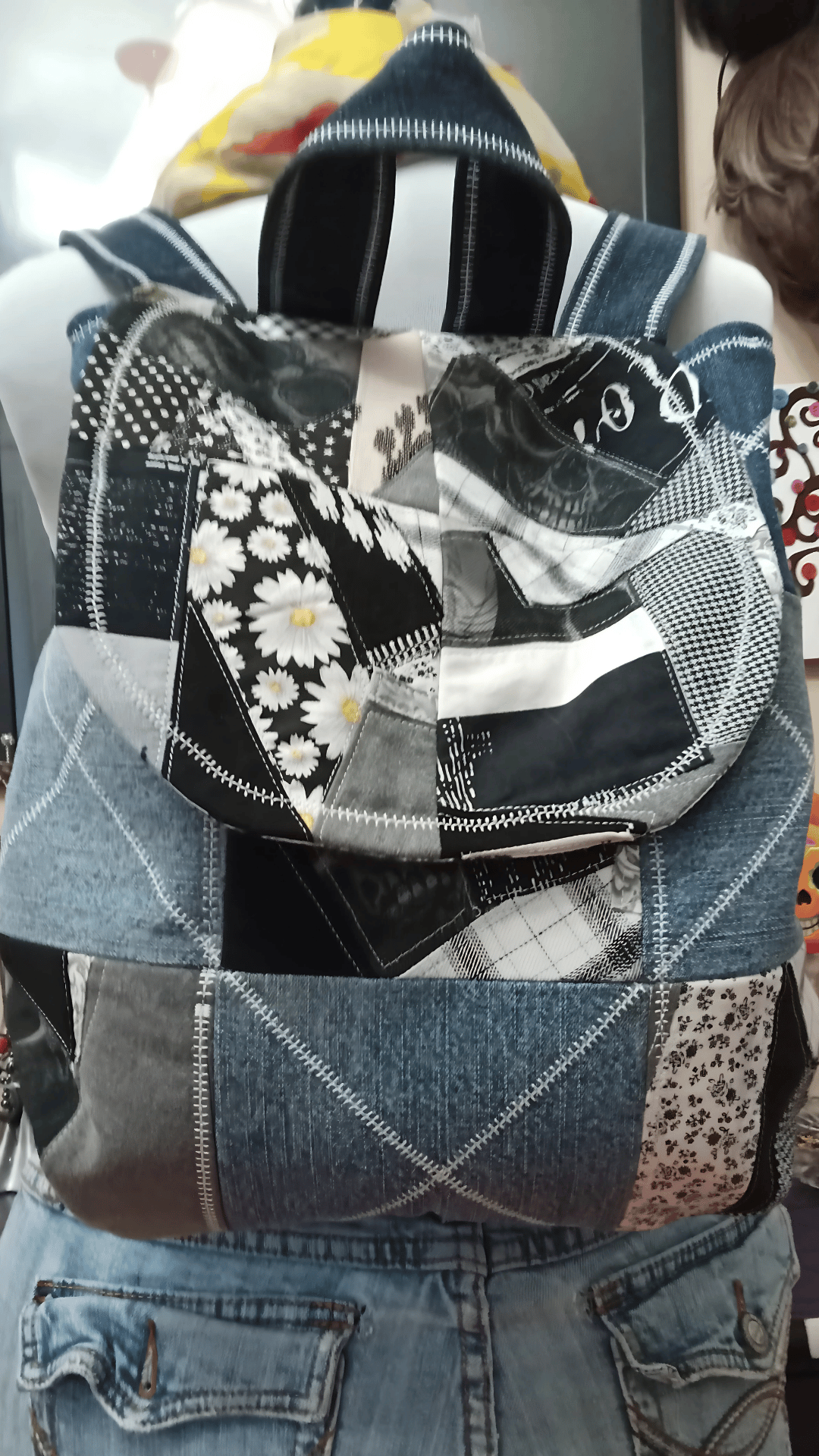 Upcycled denim backpack purse crafted from recycled blue jeans and monochromatic fabric scrap squares with decorative stitching details. This handmade patchwork backpack features layered denim textures, sustainable textile repurposing, and artistic scrap quilting inspiration.