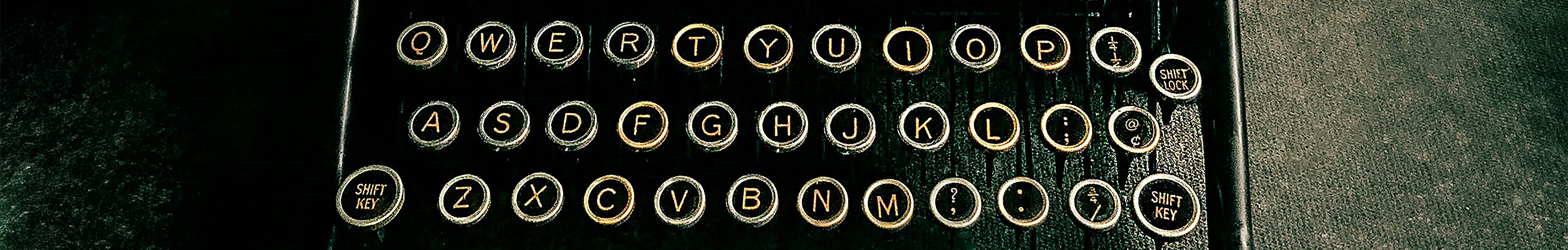 Close-up of a vintage typewriter keyboard with round black keys and gold lettering in a QWERTY layout, featured on The Creative Guide blog, showing shift keys, punctuation symbols, and textured surface detail."