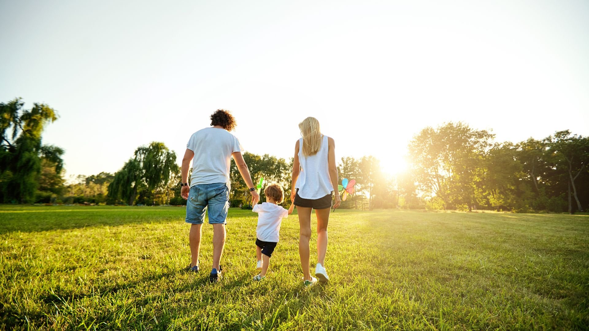 A father, mother and child walk, hand-in-hand, across a large, open, grassy field, during sunset, enjoying them selves because their finances are in order after the Financial Partner Program