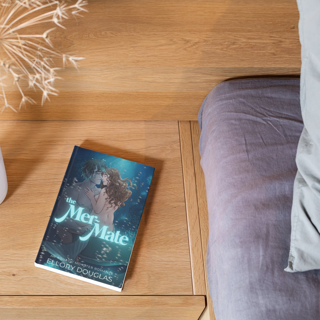 A flat lay of The Mer-Mate book on a backdrop of a wood floor with dried botanicals and bed