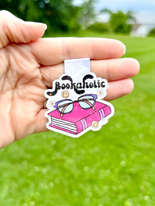 The bookmark features a cartoon design with a bright pink book, purple glasses, and the text "Bookaholic" in a playful font