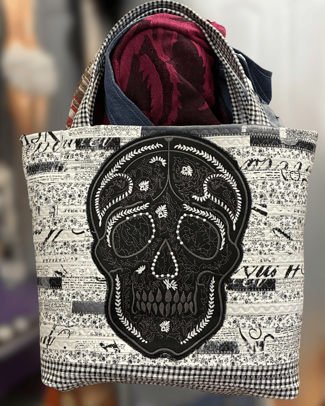 White and black upcycled jelly roll tote bag featuring a bold sugar skull appliqué with stitched detailing and bead accents. Handmade using reclaimed black and white patterned fabrics from thrifted duvet textiles, this spooky chic patchwork handbag combines gothic boho fashion, sustainable crafting, and one-of-a-kind handmade character.