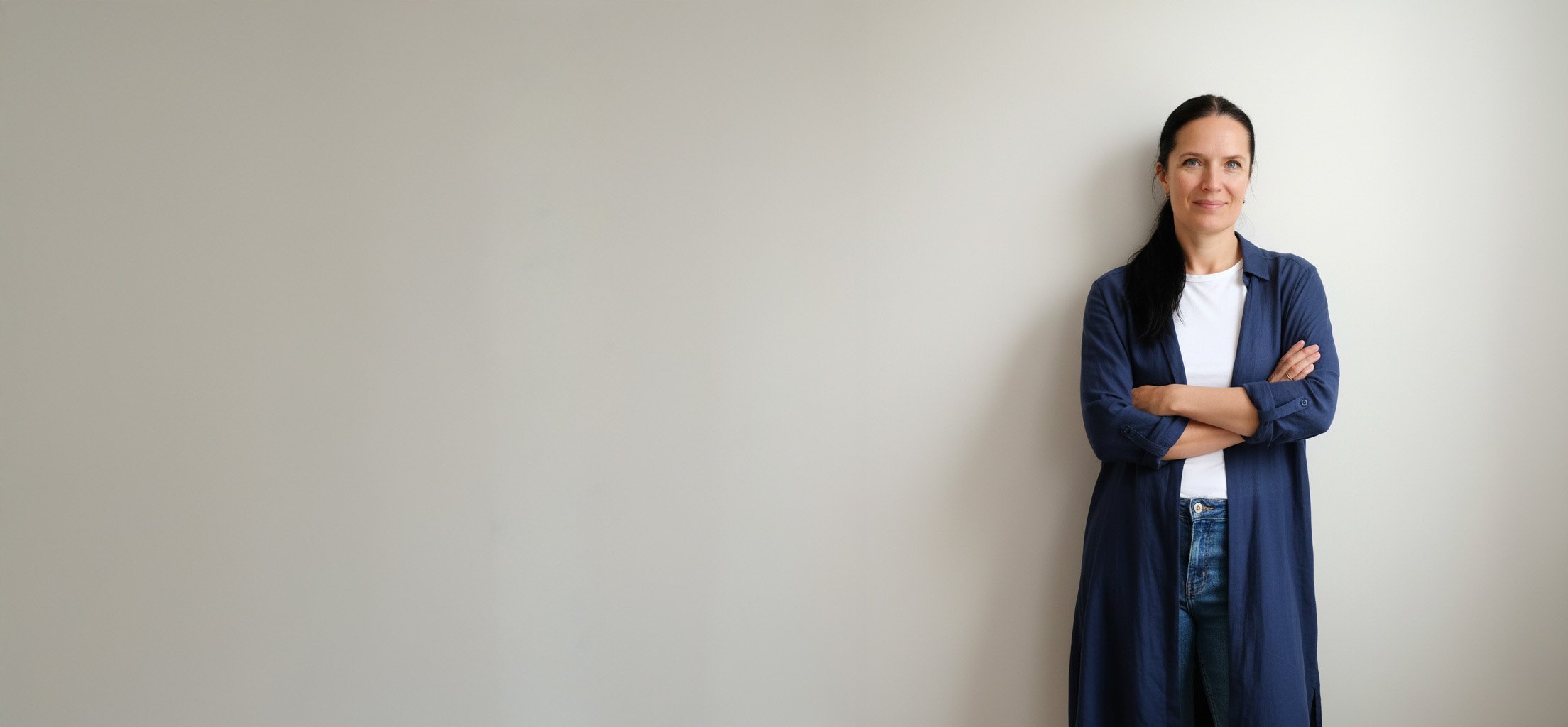 Mette standing against a white wall her amrs casually crossed smiling at a coaching client