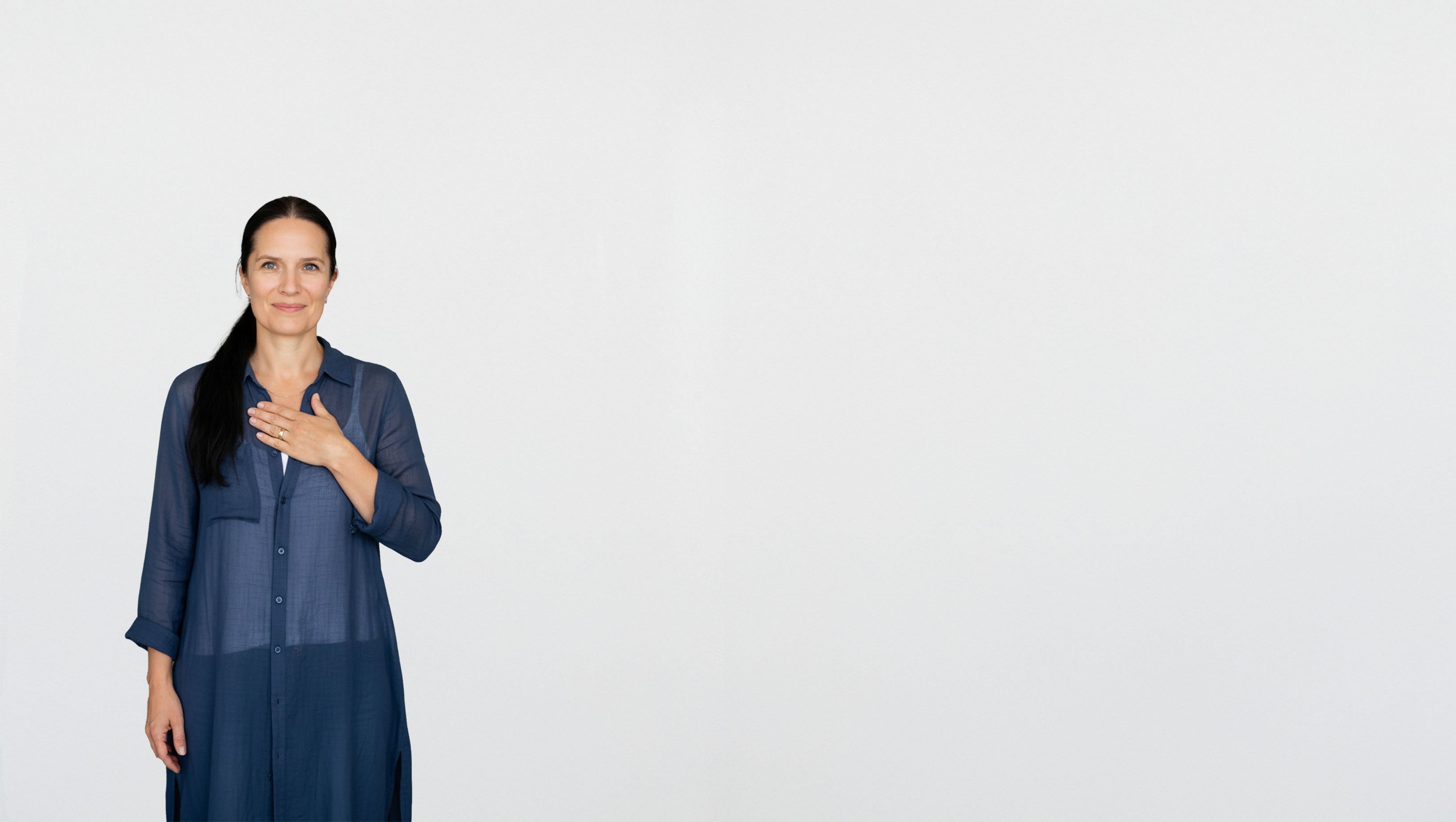Mette standing smiling against a white wall with her hand on her heart large