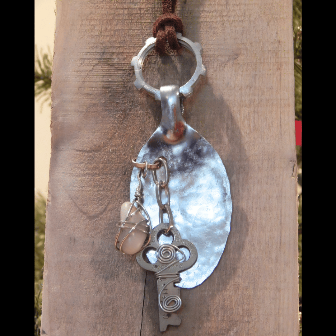 Handmade pendant crafted from a hammered spoon, featuring a wire-wrapped stone charm and a vintage key charm, created by What in Narnation.