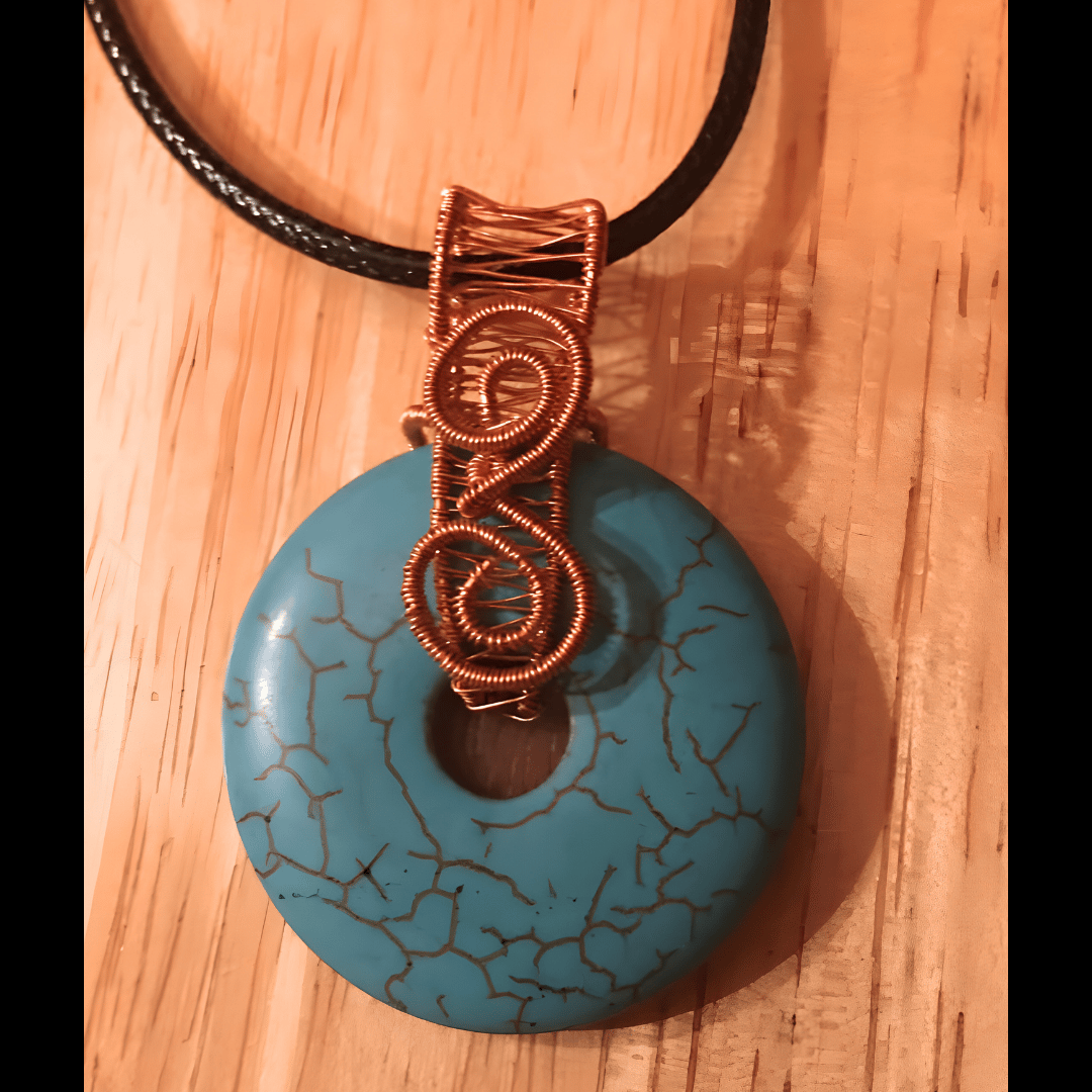 Handmade pendant featuring a blue donut-shaped stone with an intricate copper wire-wrapped bail, crafted by What in Narnation.