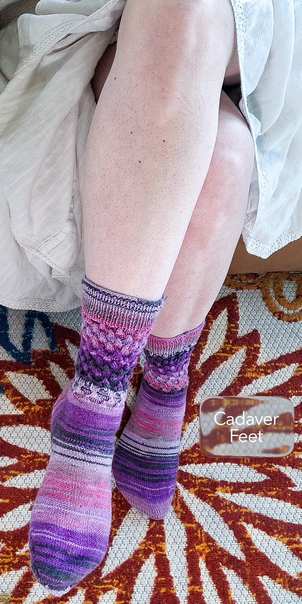 pale feet in hand-knit purple socks resting on a floral rug